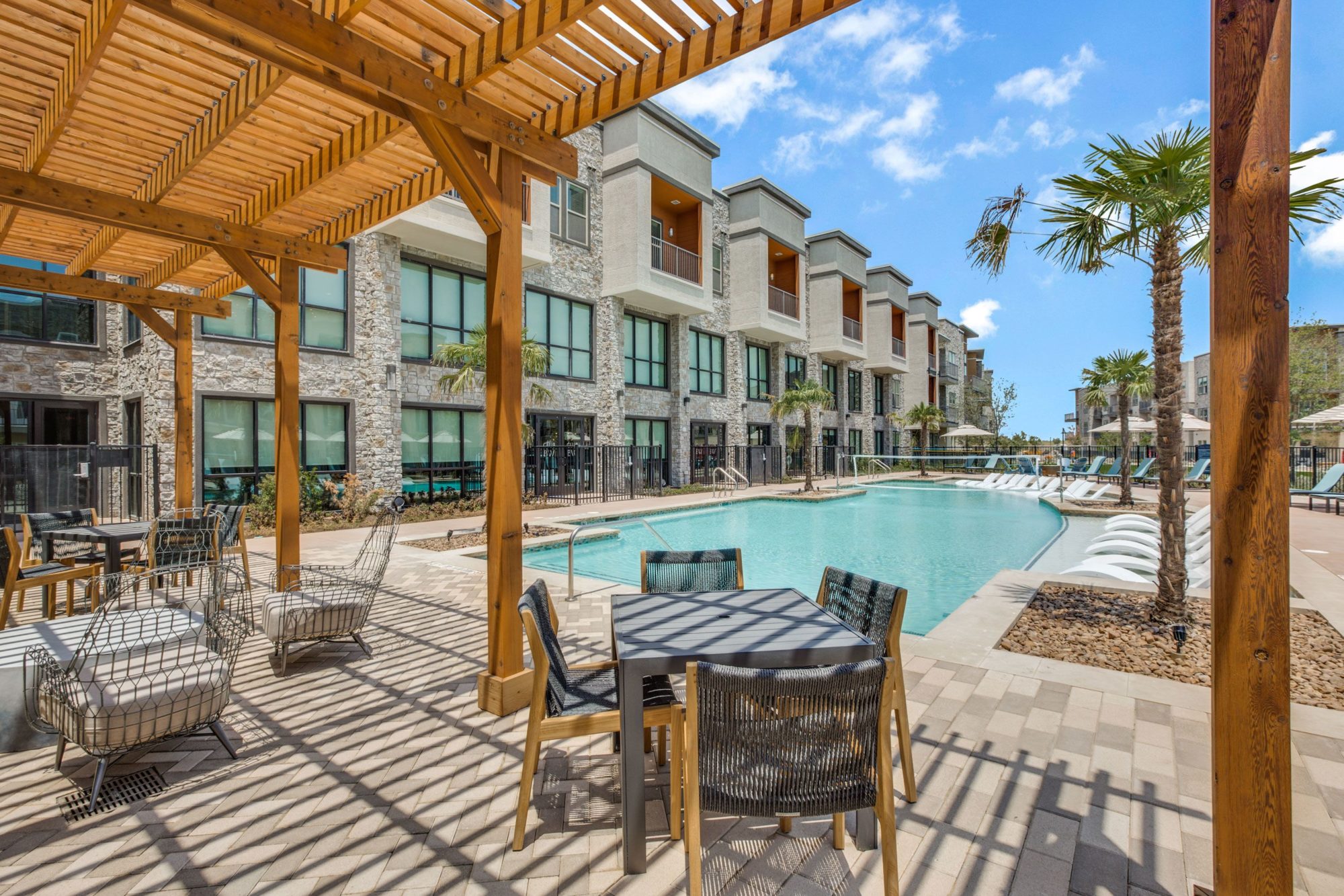 view from inside shaded pool lounge area with tables, chairs, and view of pool