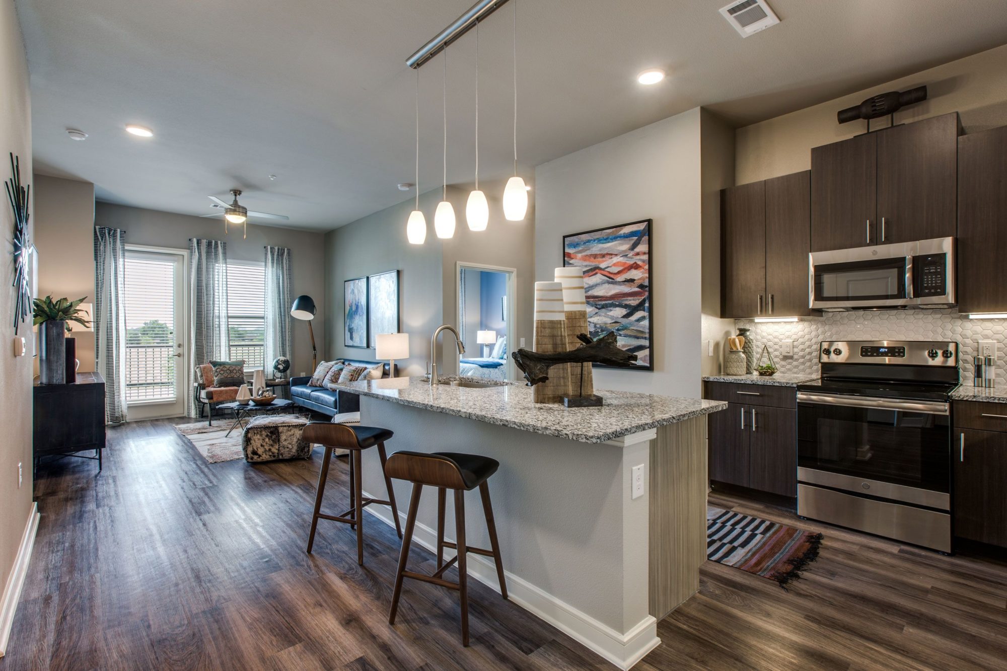 kitchen area with island, pendant lighting over island, single basin sink, wood cabinets, stove, microwave, and wood flooring