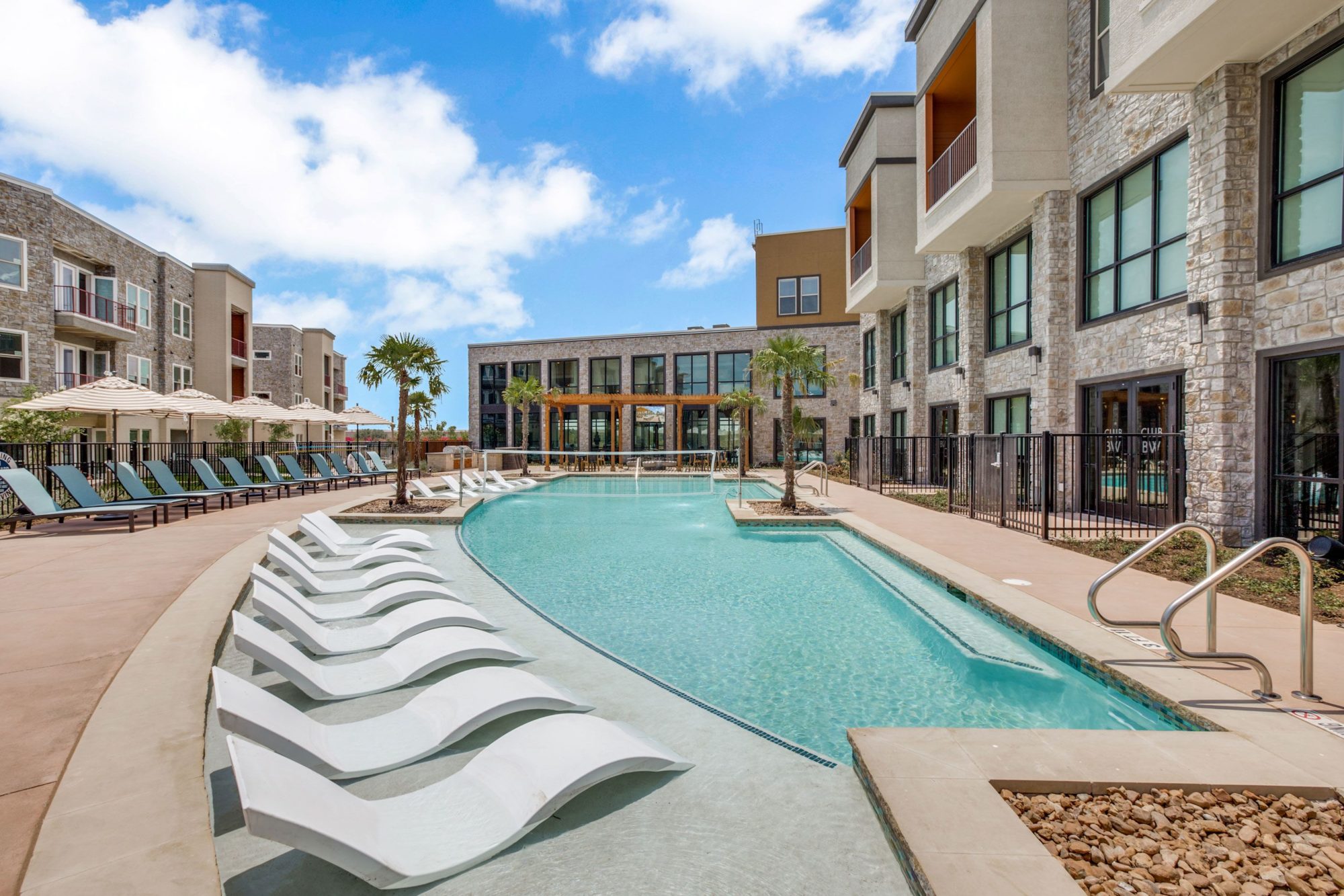 pool area with several lounge chairs, palm tress, and volley ball netting.