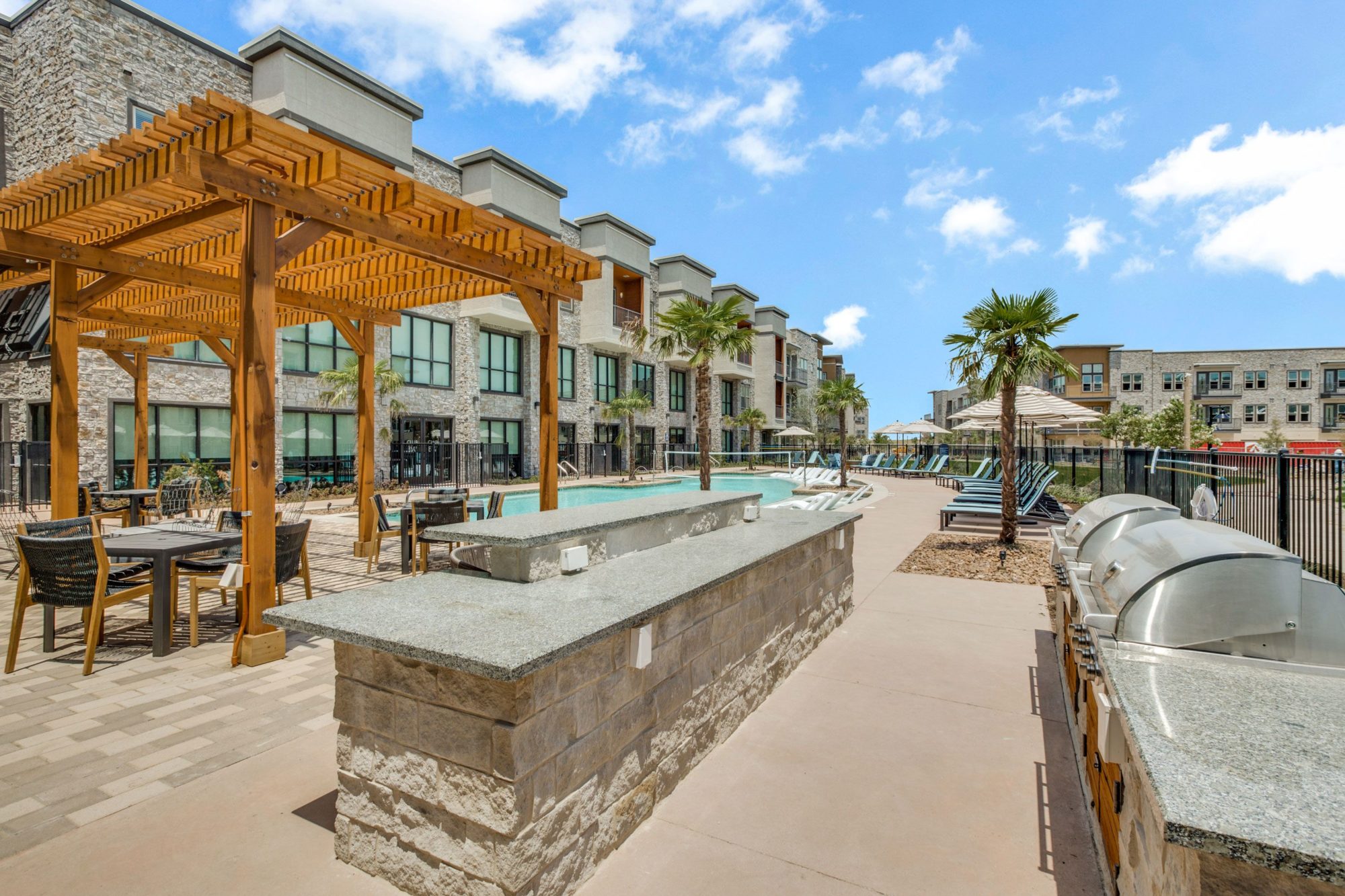 pool area with grills, stone work table, shaded lounge area, tables, chairs, and view of pool