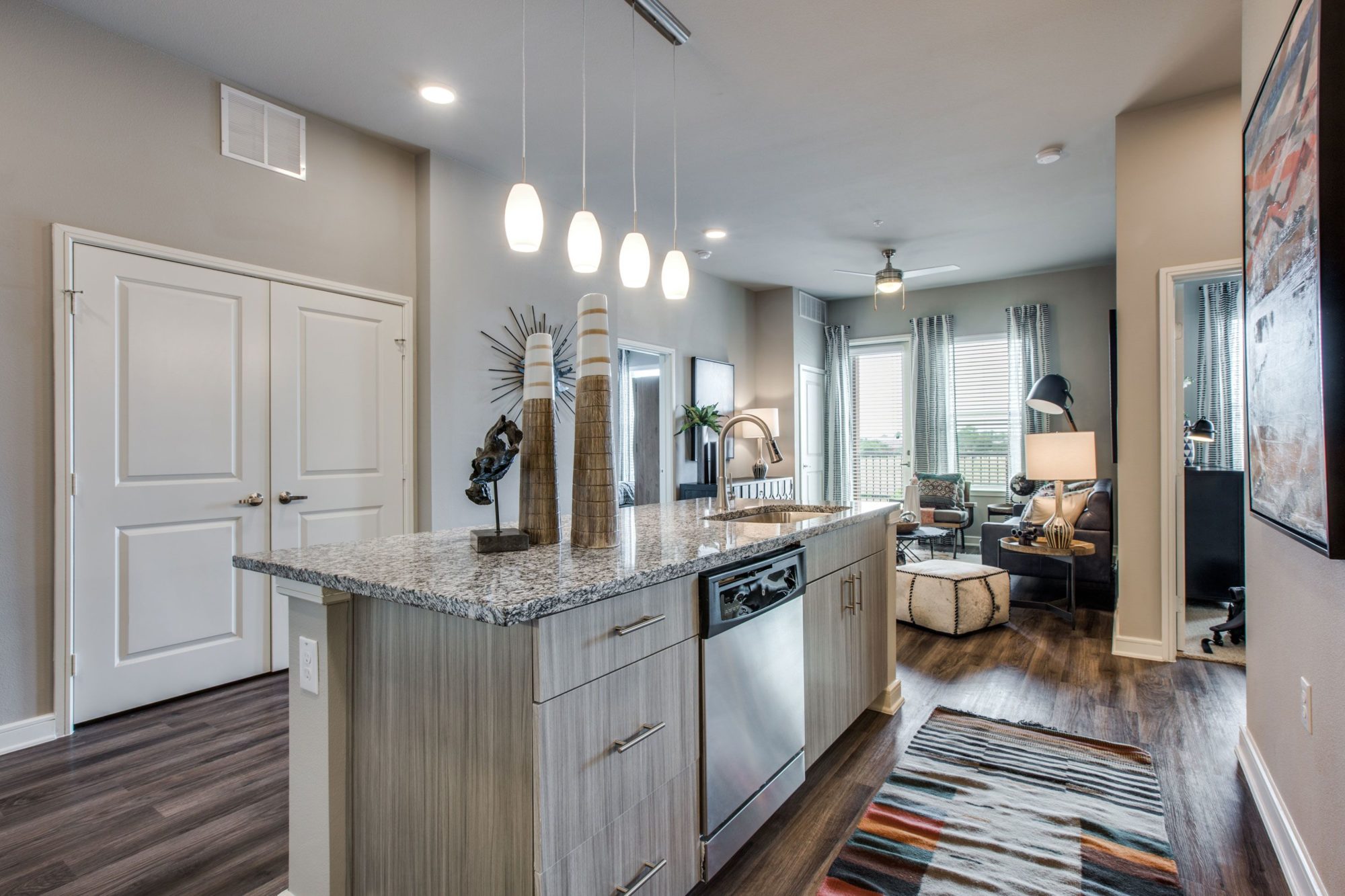 kitchen with island, dishwasher, wood cabinets, wood flooring, granite countertops, and view of living area