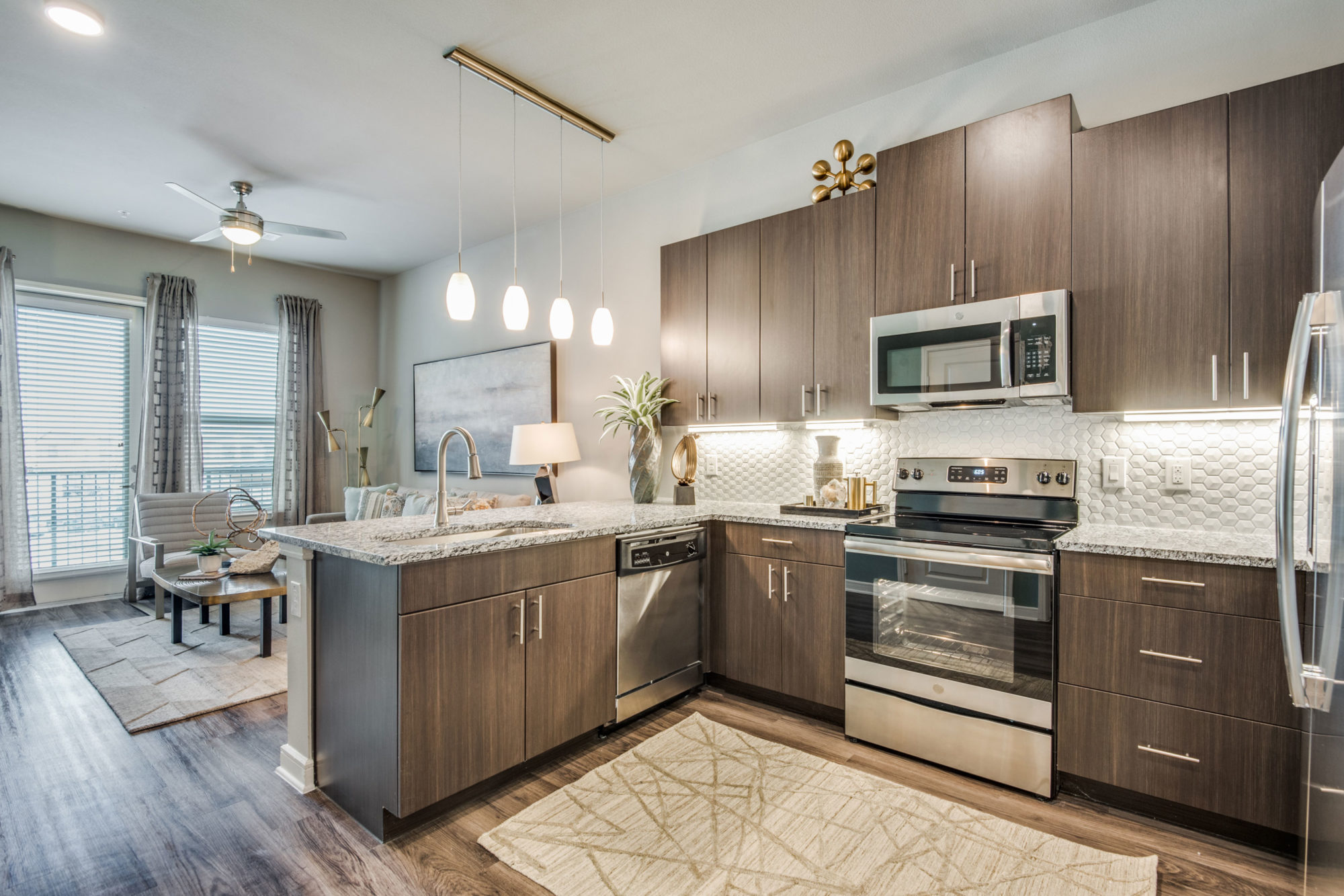 l-shaped kitchen with wood cabinets, stove, microwave, pendant lighting over bar, and single basin sink