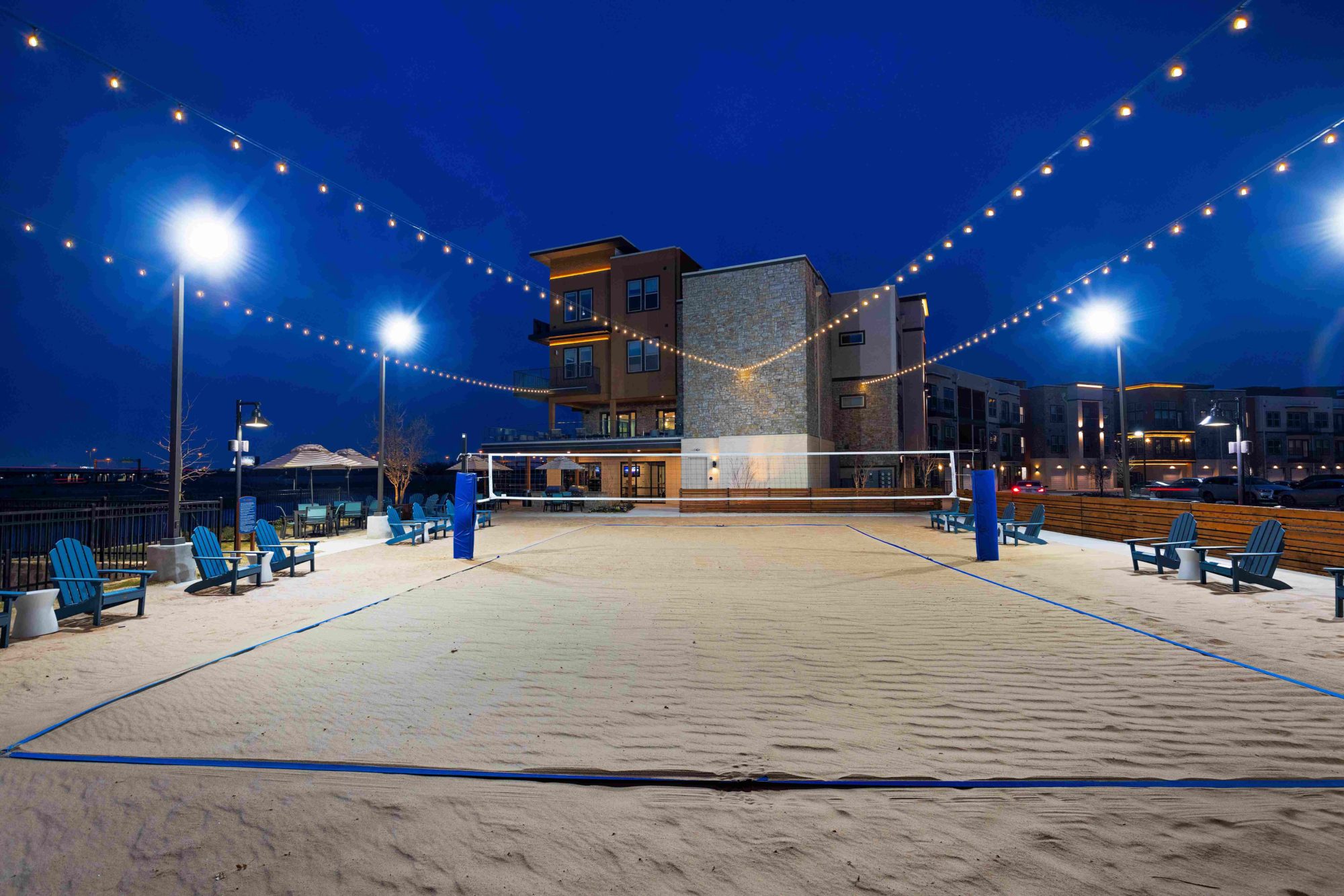 night shot of sand volleyball court with string lighting and property buildings in the background
